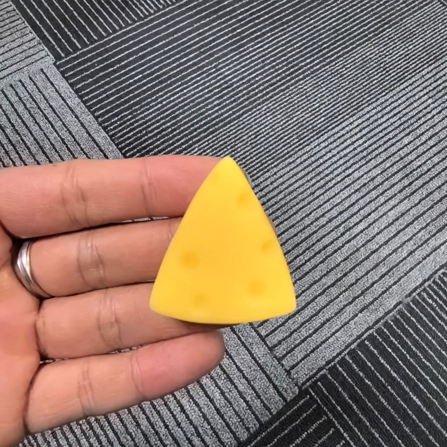 cheese squishy, Yellow triangular sponge held in a hand on a textured gray surface