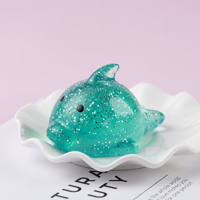 Purple Mochi Squishy, Turquoise glittery dolphin toy on a white shell with a light purple background